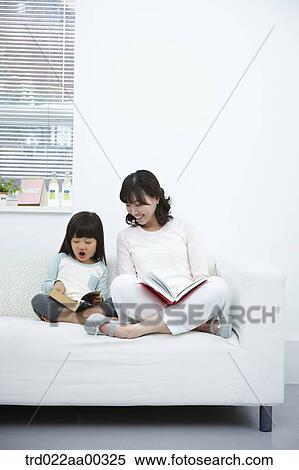 Stock Photography - The woman and girl reading a book together on the couch. Fotosearch