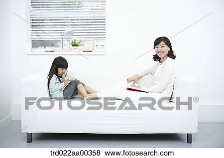 Stock Photo - The woman and girl sitting on the couch with the book. Fotosearch