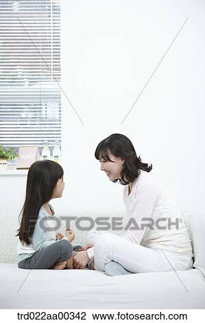 Stock Image - The woman and girl smiling at each other on the couch. Fotosearch