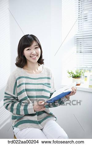 Picture - The woman holding a book by the window. Fotosearch