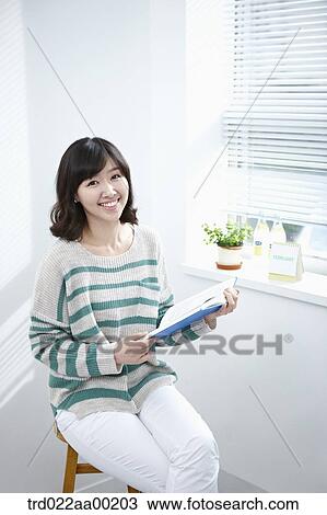 Stock Image - The woman holding a book by the window. Fotosearch