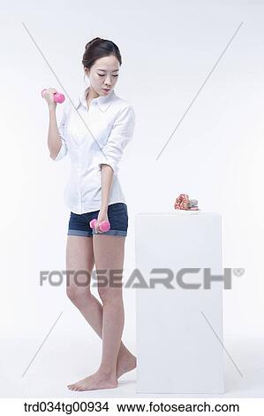 Picture - The woman looking at the doughnuts while exercising with dumbbells . Fotosearch