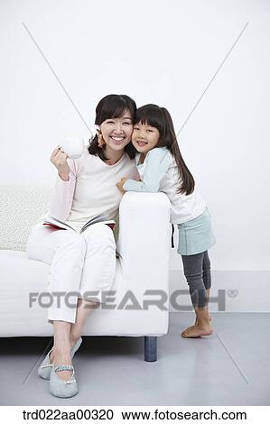 Stock Image - The woman on the couch and the girl hugging the woman. Fotosearch