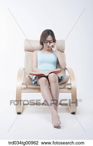Stock Image - The woman reading a book on the chair. Fotosearch