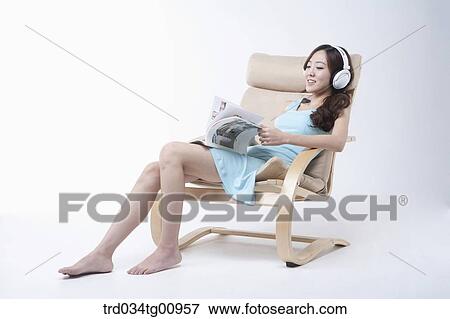 Stock Photo - The woman reading magazine on the chair with the headphone on . Fotosearch