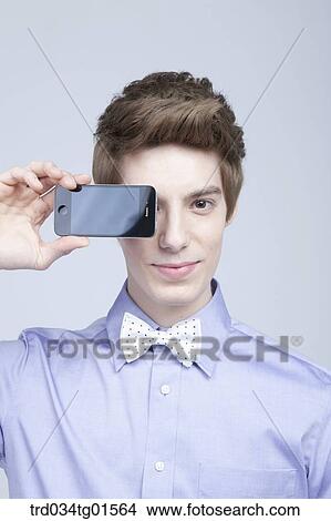 Picture - A man holding the smart phone over his face . Fotosearch