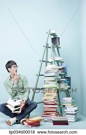 Stock Photo - A man looking at the piled books. Fotosearch