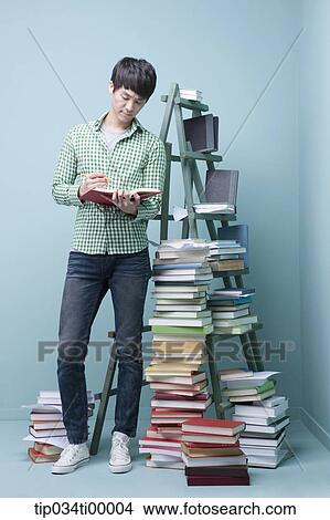 Picture - A man reading a book by the piled books and ladder. Fotosearch
