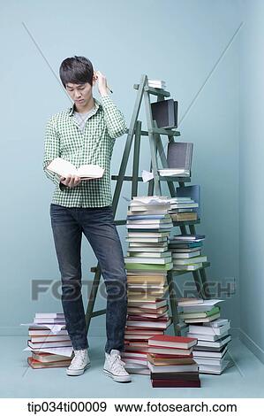 Stock Photo - A man reading a book by the piled books and ladder. Fotosearch