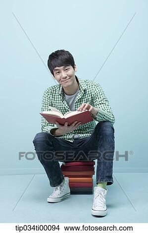 Picture - A man reading a book on the piled books. Fotosearch