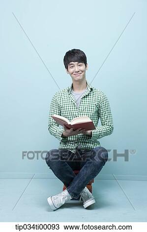 Stock Image - A man reading a book on the piled books. Fotosearch