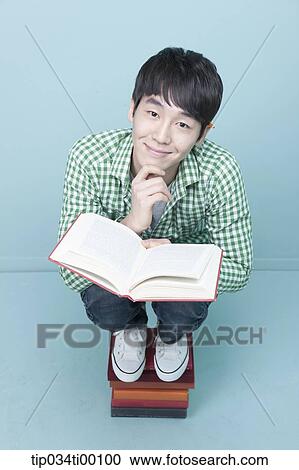 Stock Image - A man reading a book on the piled books. Fotosearch