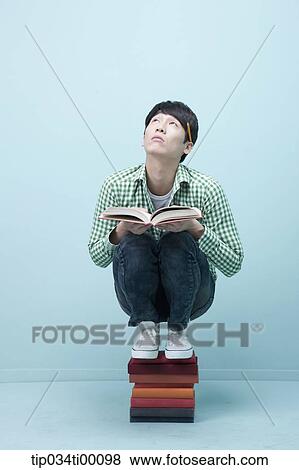 Stock Photo - A man reading a book on the piled books. Fotosearch