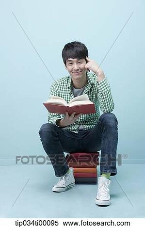 Stock Photography - A man reading a book on the piled books. Fotosearch