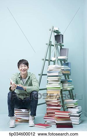 Stock Image - A studying man by the piled books and ladder. Fotosearch