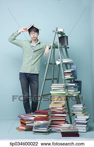 Stock Image - A studying man by the piled books and ladder. Fotosearch