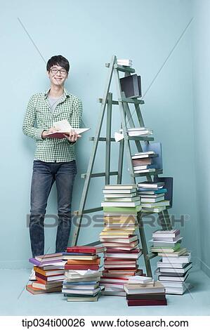 Stock Photograph - A studying man by the piled books and ladder. Fotosearch