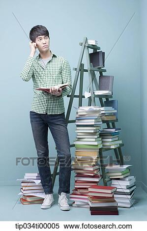 Stock Photography - A studying man by the piled books and ladder. Fotosearch