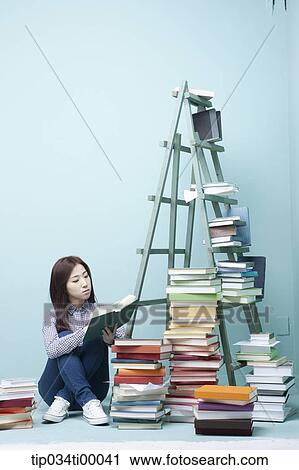 Stock Image - A studying woman by the piled books and ladder. Fotosearch