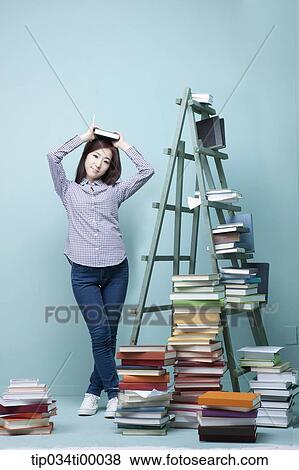 A woman holding up a book by the piled books and ladder View Large Photo Image Stock Photo - A woman holding up a book by the piled books and ladder. Fotosearch
