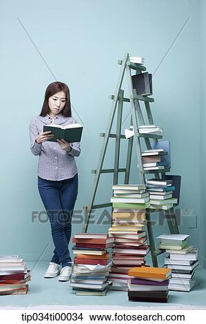 A woman reading a book by the piled books and ladder View Large Photo Image Picture - A woman reading a book by the piled books and ladder. Fotosearch