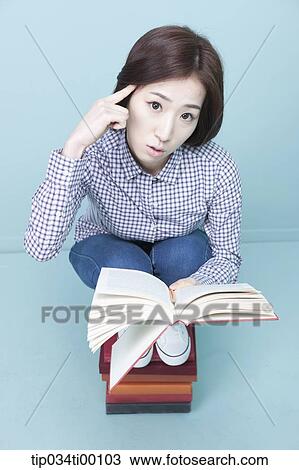 Stock Image - A woman reading a book on the piled books. Fotosearch