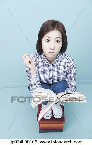 Stock Photograph - A woman reading a book on the piled books. Fotosearch