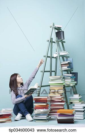 Stock Image - A woman reading out for the book on the ladder. Fotosearch