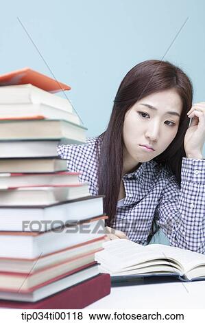Stock Photo - A woman worrying about the piled books. Fotosearch