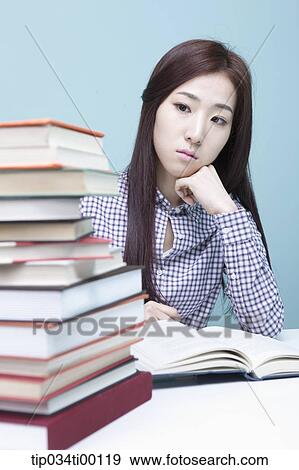 Stock Photo - A woman worrying about the piled books. Fotosearch