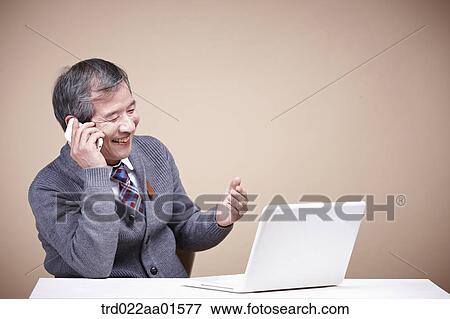 An old man talking on the phone while looking at laptop View Large Photo Image Stock Photo - An old man talking on the phone while looking at laptop . Fotosearch