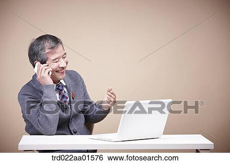 Stock Photograph - An old man talking on the phone while looking at laptop . Fotosearch