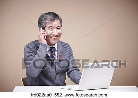 Stock Image - An old man talking on the phone with the laptop around. Fotosearch