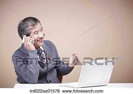 Stock Photo - An old man talking on the phone with the laptop around. Fotosearch