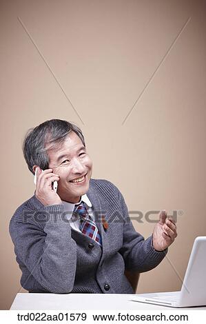 Stock Photo - An old man talking on the phone with the laptop around. Fotosearch