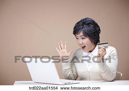 Picture - An old woman surprised at laptop monitor with credit card. Fotosearch