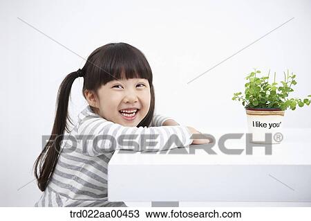 Smiling girl with green plant on the table View Large Photo Image Stock Image - Smiling girl with green plant on the table. Fotosearch