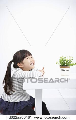 Stock Image - Smiling girl with green plant on the table. Fotosearch