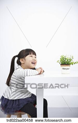 Smiling girl with green plant on the table View Large Photo Image Stock Photo - Smiling girl with green plant on the table. Fotosearch