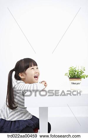 Stock Photo - Smiling girl with green plant on the table. Fotosearch