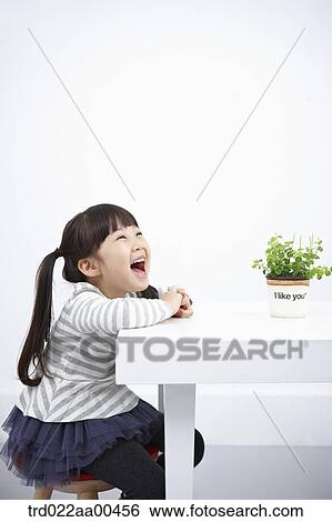 Stock Photograph - Smiling girl with green plant on the table. Fotosearch