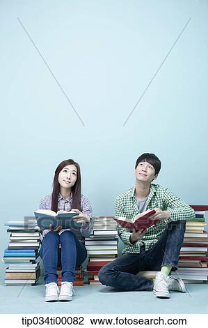 Stock Image - Studying man and woman between the piled books. Fotosearch
