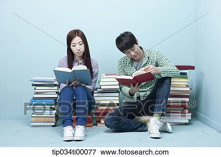 Stock Photo - Studying man and woman between the piled books. Fotosearch