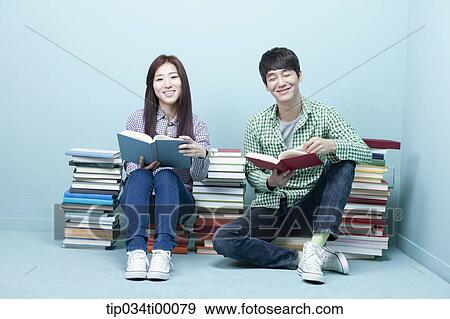 Stock Photo - Studying man and woman between the piled books. Fotosearch