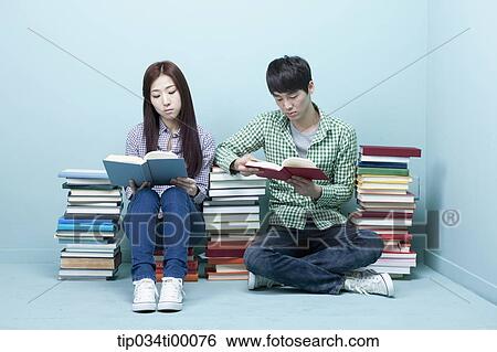 Stock Photograph - Studying man and woman between the piled books. Fotosearch