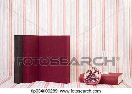 Stock Photo - The red and brown cover book, glass bottle, and pomegranate . Fotosearch