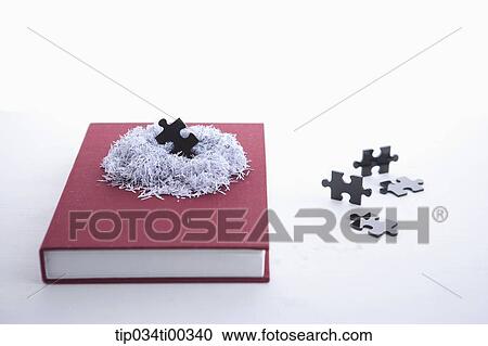 Stock Image - The shredded paper on the book and the pieces of puzzle. Fotosearch