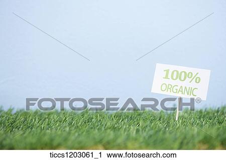 Stock Image - 100 percent organic sign fixed on a grass. Fotosearch