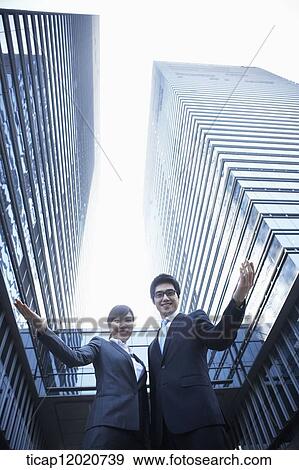 Stock Photo - A business man and a business woman watching down towards the camera holding their hands up. Fotosearch