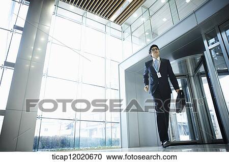 Stock Image - A business man with a briefcase man running into an office building . Fotosearch